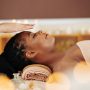 Therapist holding hands over head of pretty young Black woman to transfer energy during healing reiki session